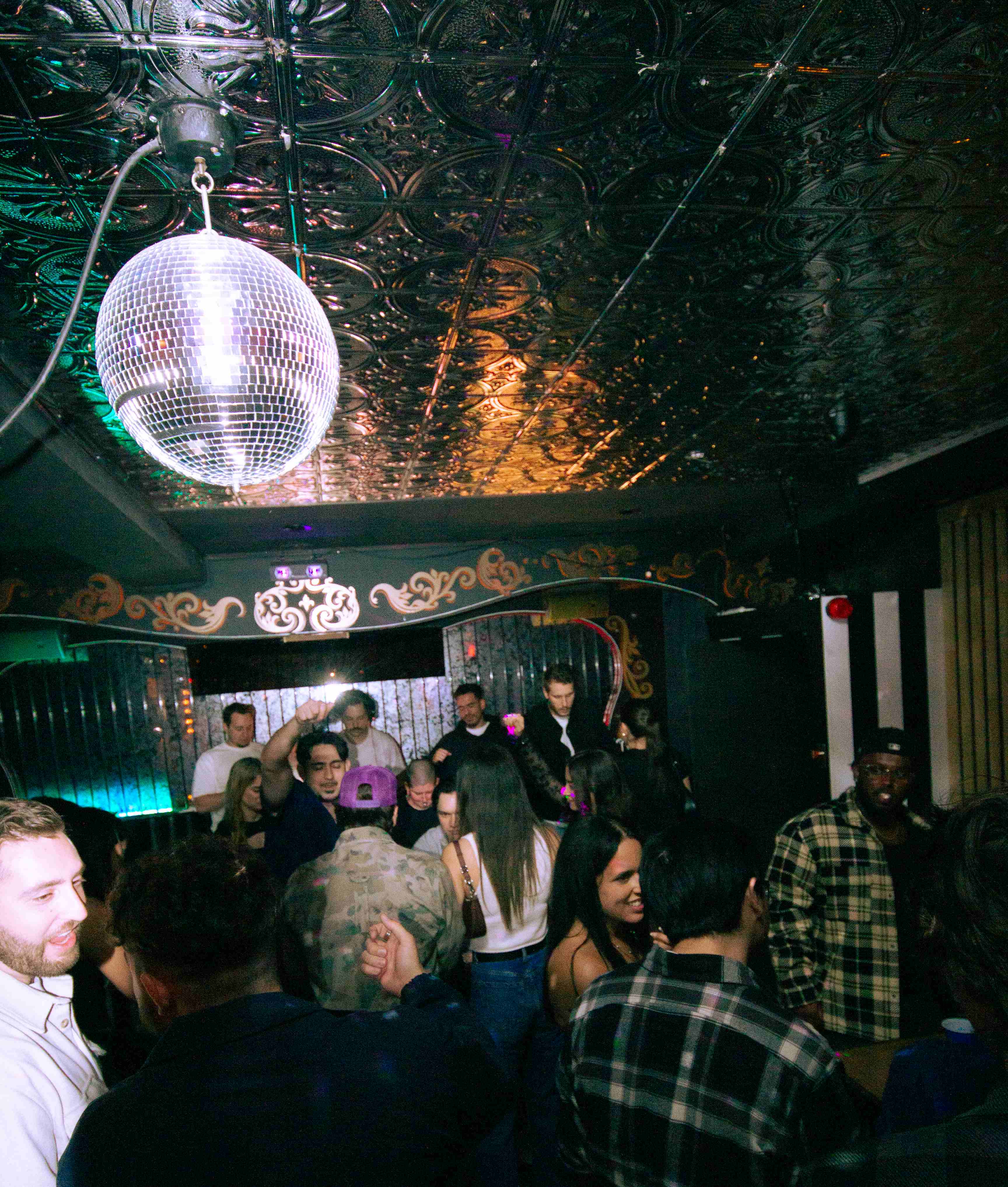 Une piste de danse pleine sous la boule disco et le plafond en tôle ouvragée